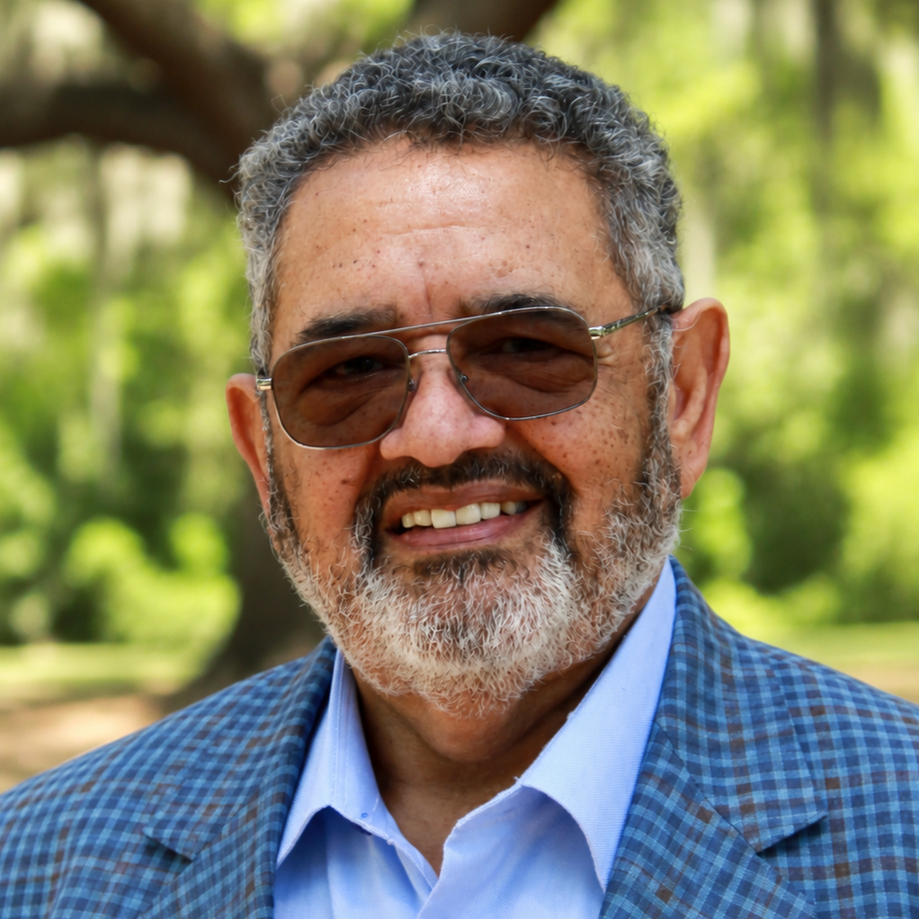 Bearded man wears sunglasses and a blue checkered suit